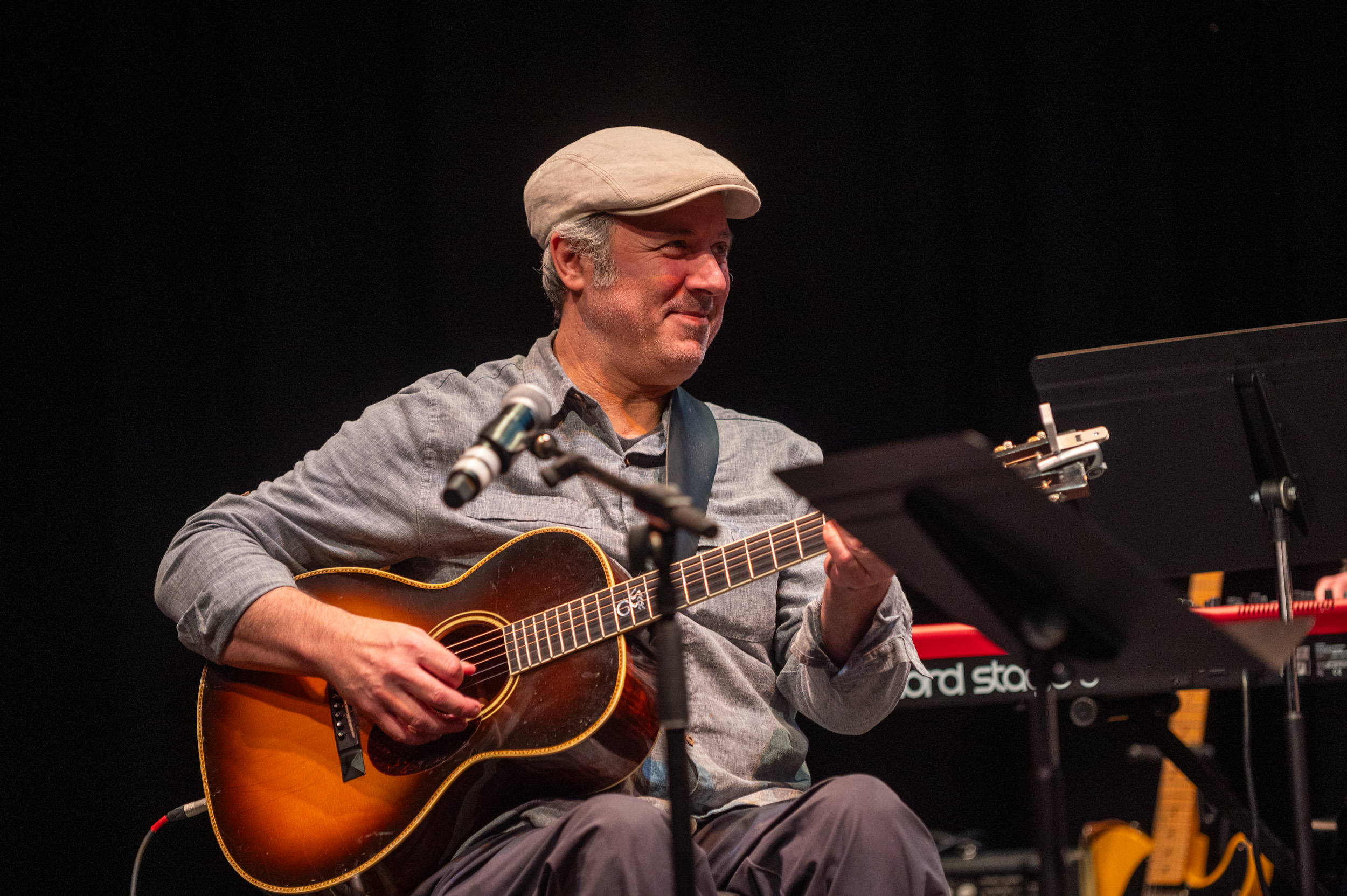 Photo of Simon Paradis on stage at the 2024 Strong Sessions. He is smiling and holding an acoustic guitar.